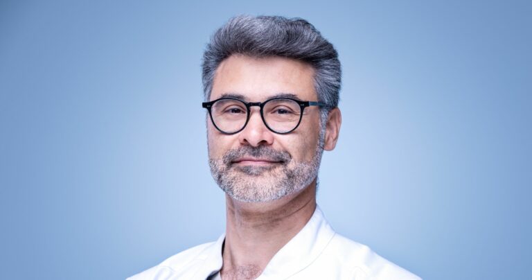 Portrait corporate d'un homme souriant à lunettes sur fond bleu clair, portrait professionnel en studio