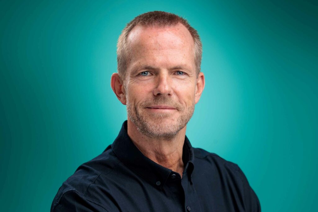 Headshot d'un homme en chemise noire sur fond turquoise
