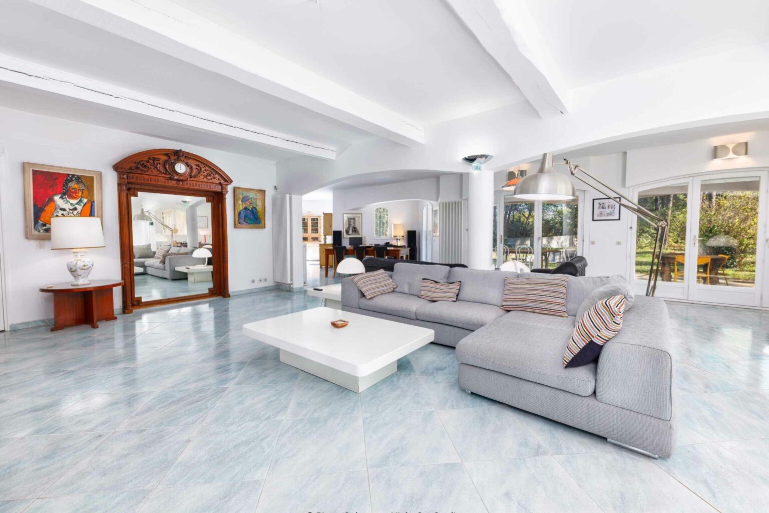 Grand séjour lumineux avec sol en marbre, canapés blancs et porte voûtée, photographie immobilière
