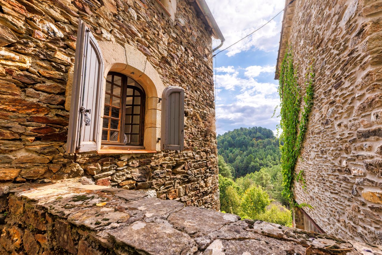 Fenêtre cintrée d'un mas en pierre de schiste avec vue sur les crêtes boisées des Cévennes