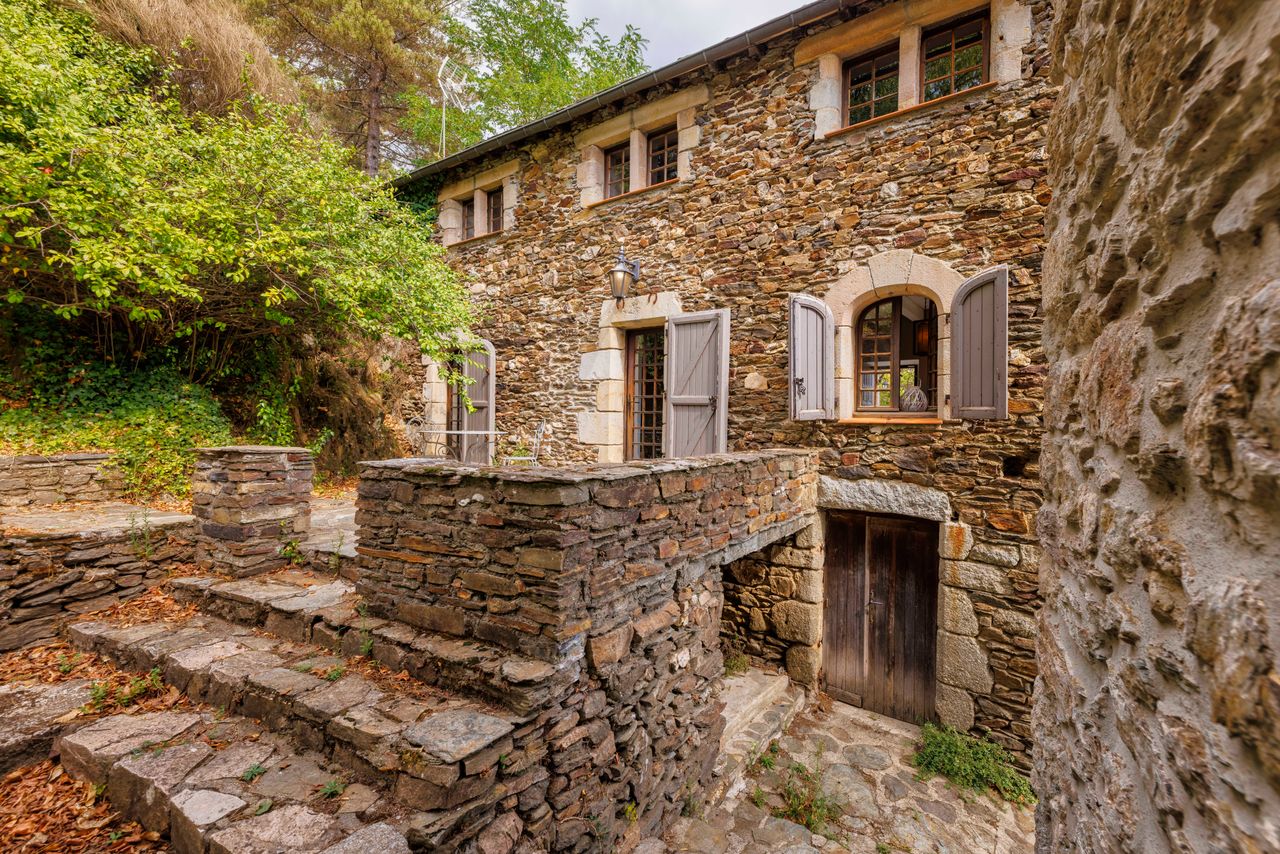 Façade d'un mas cévenol en pierre de schiste à Génolhac, escaliers en pierre et volets en bois