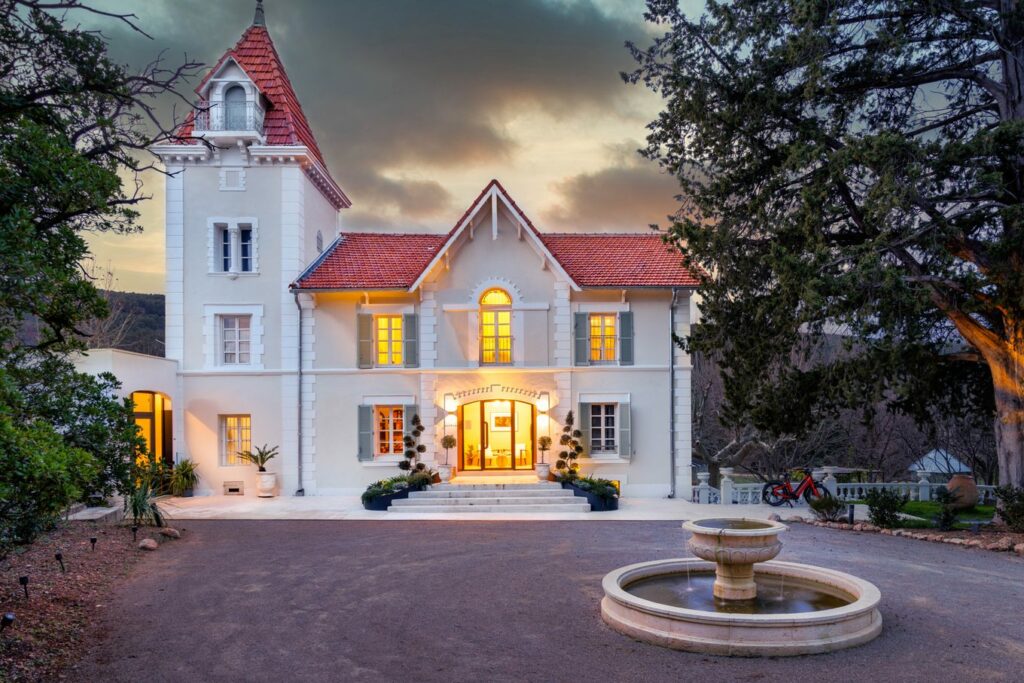 Façade du château Pimo éclairée au crépuscule, cour et fontaine au premier plan