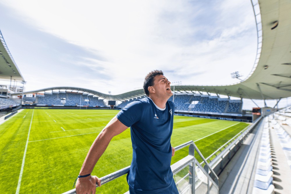 Photographe sportif : Arthur Vincent, rugbyman du XV de France, en polo bleu dans les tribunes d'un stade de rugby