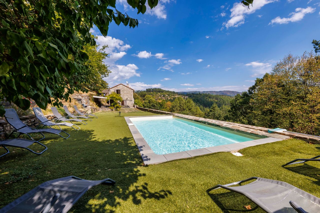Piscine sur pelouse avec transats face à la vallée boisée, domaine à Génolhac