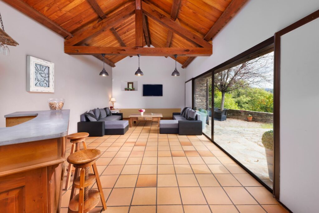 Salon sous charpente apparente en bois avec baie vitrée ouverte sur la terrasse, mas à Génolhac