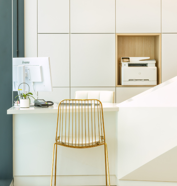 Photo d'un espace de bureau, contenant une imprimante, une chaise couleur dorée et un rideau vert sur la gauche.